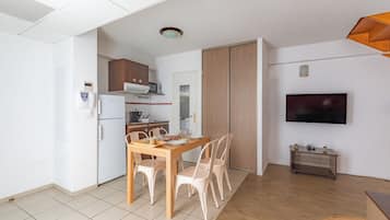 A modern kitchen with white cabinets, a dining table with chairs, a TV mounted on the wall, and a small cart with plants.