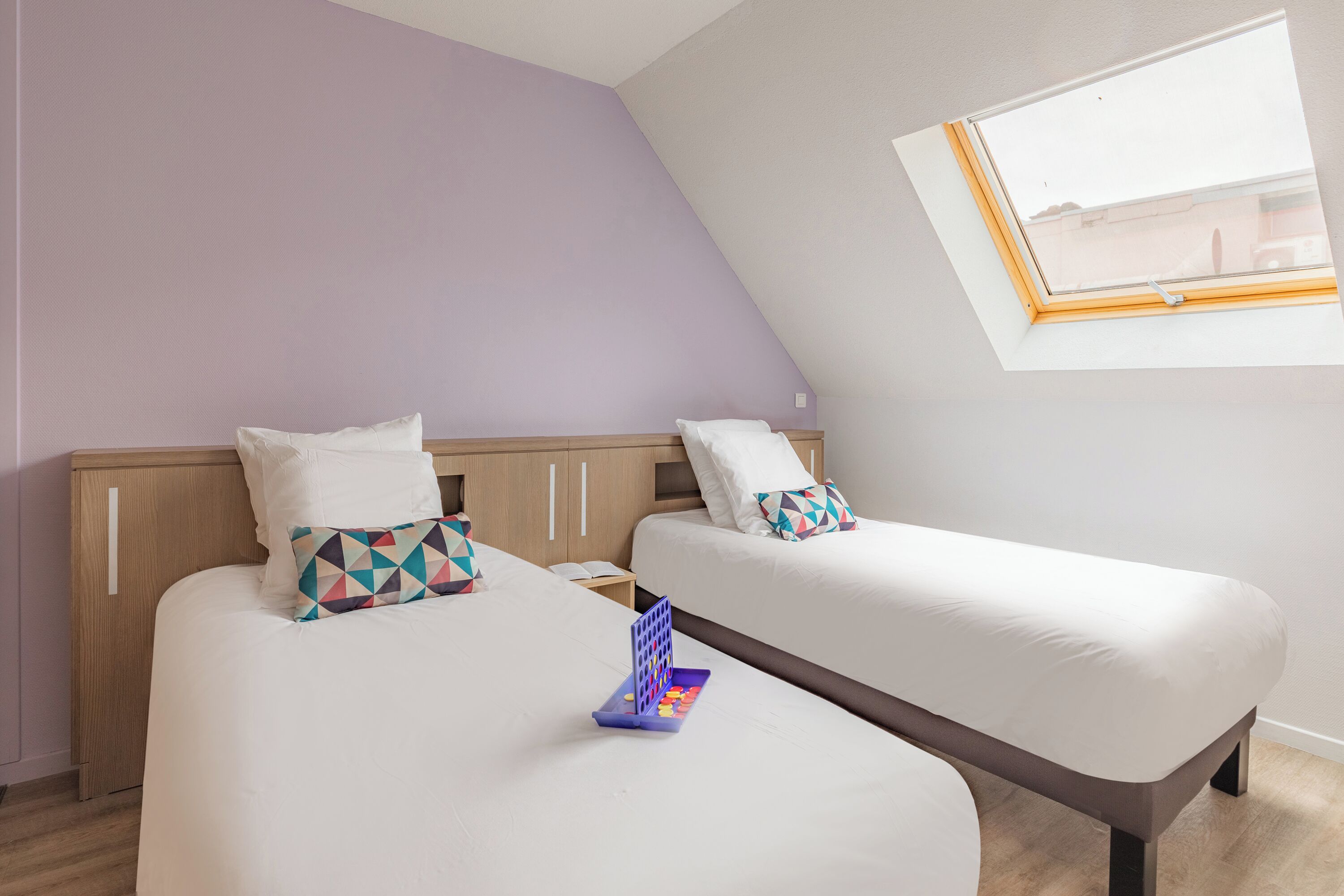 Une chambre avec deux lits, une fenêtre et une petite table sur laquelle se trouve un plateau.