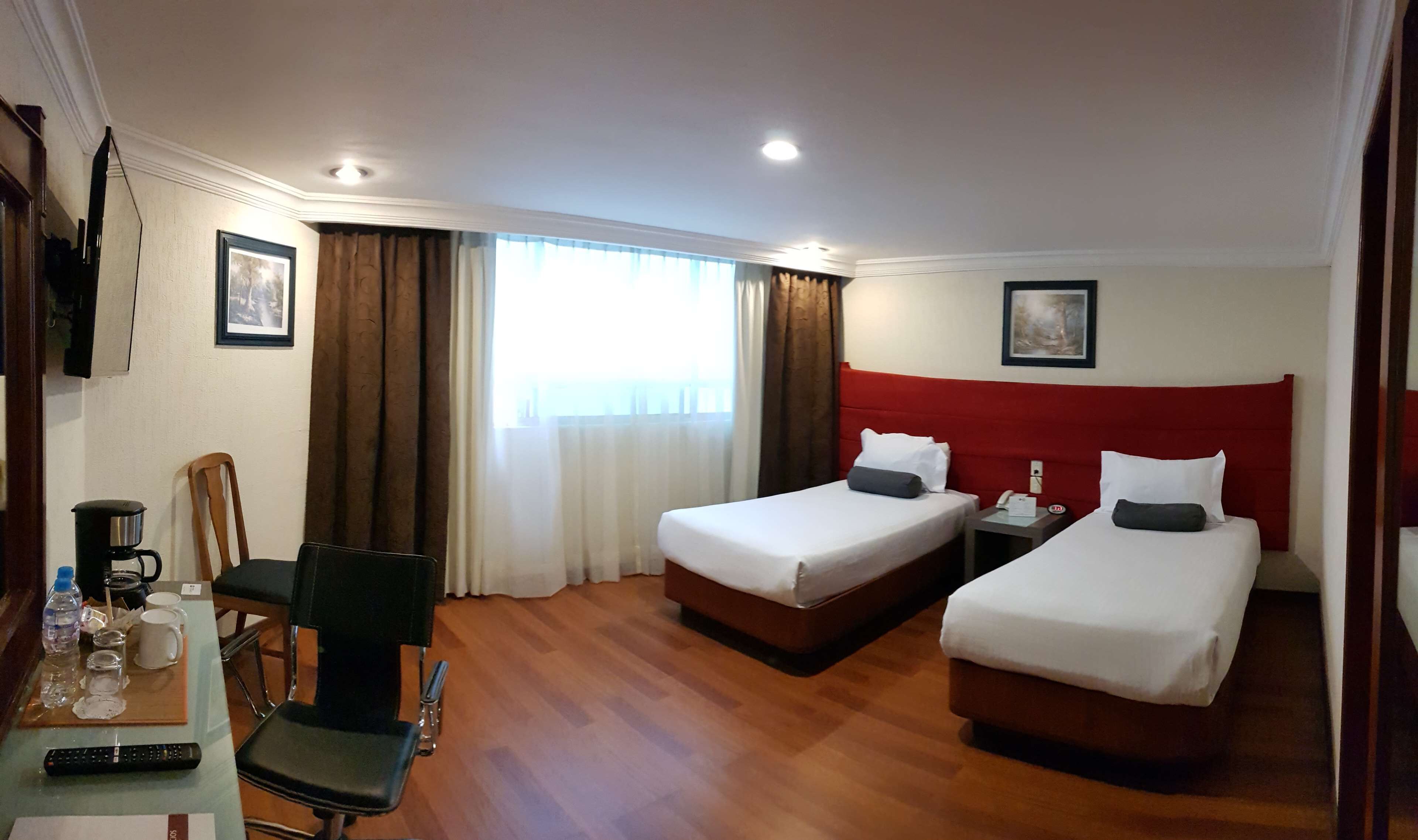 A hotel room with two beds, a desk with a coffee maker, a chair, and a TV.