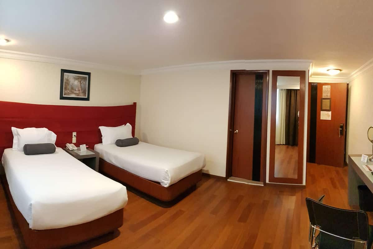 Une chambre d’hôtel avec deux lits, un bureau, une chaise et un miroir.
