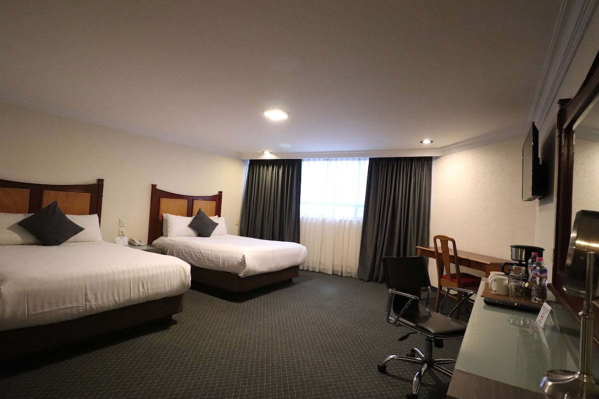Une chambre d’hôtel avec deux lits, un bureau avec une chaise, une télévision et une fenêtre avec des rideaux.