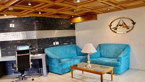 Uma área de recepção com um sofá azul, uma mesa de centro de madeira, uma mesa com um computador e um design de teto moderno.