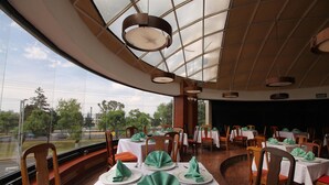 Restaurante com mesas redondas, guardanapos verdes e vista para o exterior.
