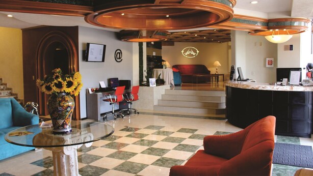 Um saguão com piso xadrez, balcão de recepção, um sofá e uma mesa de centro com um vaso.