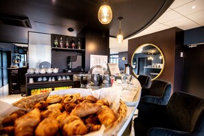 A café with a variety of pastries displayed in the foreground, a coffee bar in the background, and a mirror on the wall. - Brit Hotel Du Stade (Rennes)