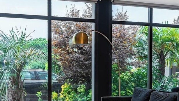 A modern living room with a dark sofa, a brown armchair, and a coffee table. There is a large window with a view of greenery and a car outside. - Brit Hotel Du Stade (Rennes)