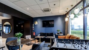 A modern lounge area with a foosball table, comfortable seating, a large TV, and a view through the window. - Brit Hotel Du Stade (Rennes)