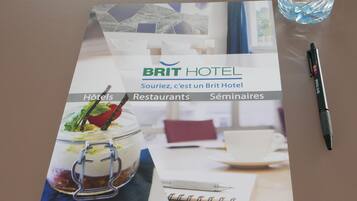Un folleto de Brit Hotel con secciones sobre hoteles, restaurantes y seminarios. También se aprecia una botella de agua y un bolígrafo.
