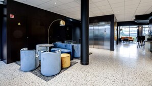 A modern lobby with seating areas, a large pillar, and an elevator. - Brit Hotel Du Stade (Rennes)