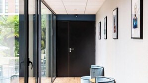 A modern reception area with a wooden floor, a brown leather sofa, and a glass wall with a view of the outdoors. - Brit Hotel Du Stade (Rennes)