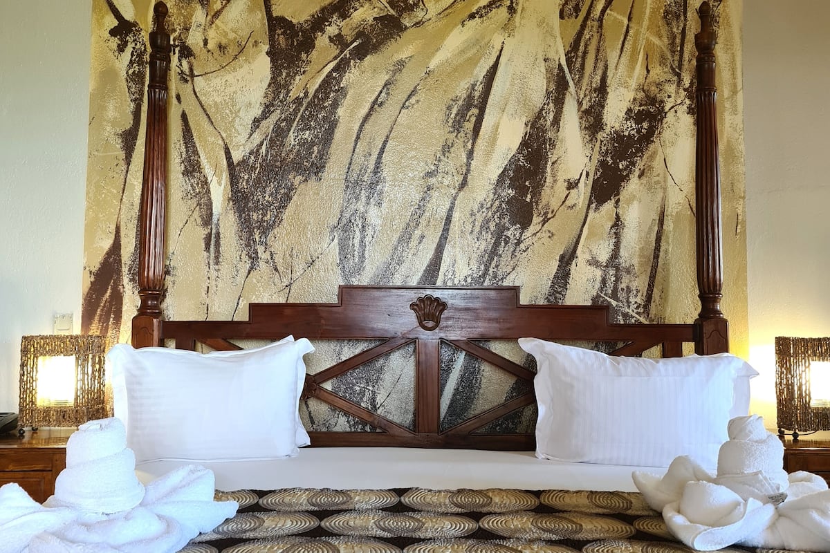Un lit avec une tête de lit en bois, des oreillers blancs et un grand tableau abstrait accroché au mur derrière.