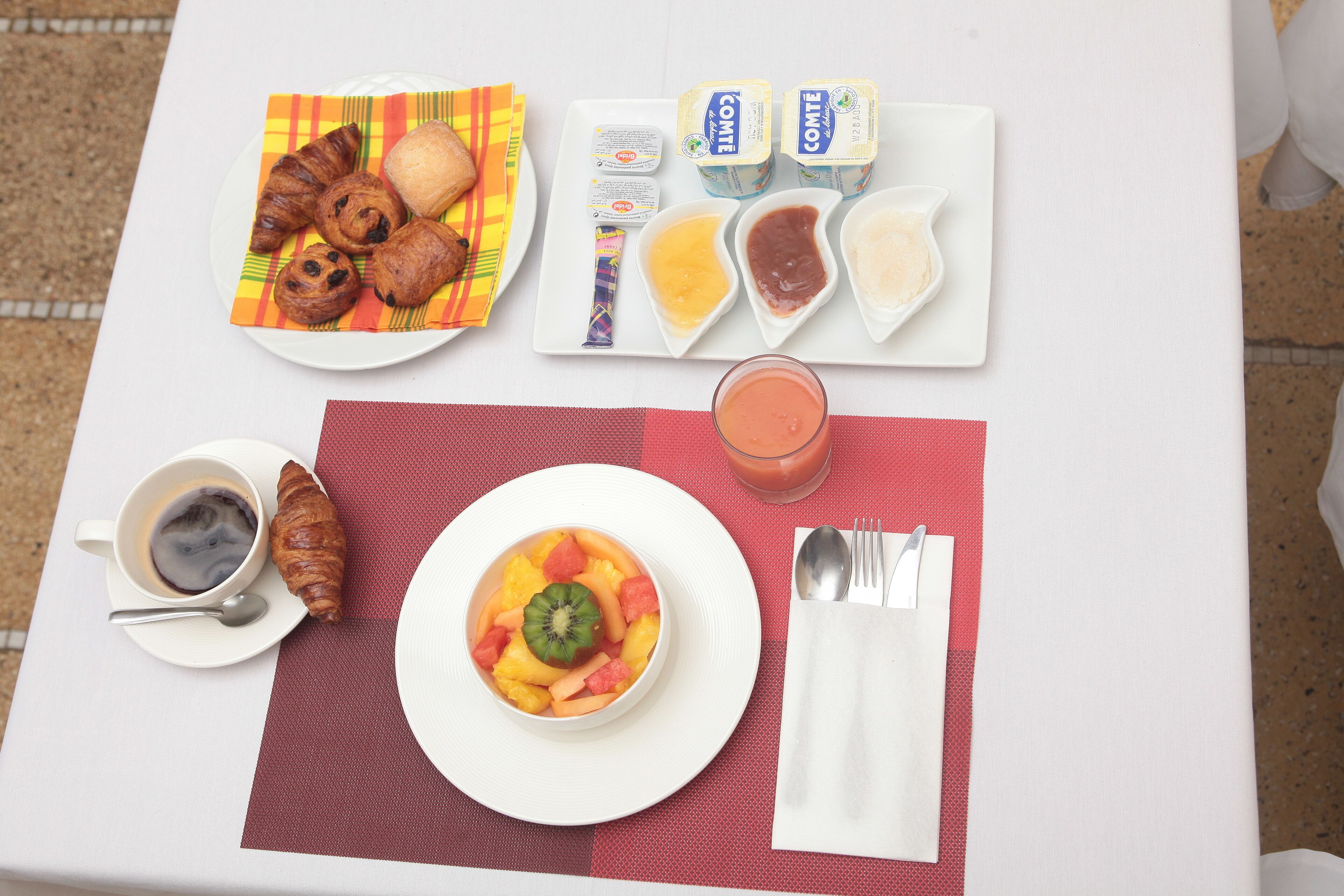 Una mesa de desayuno con cruasanes, fruta, yogur y un vaso de jugo.