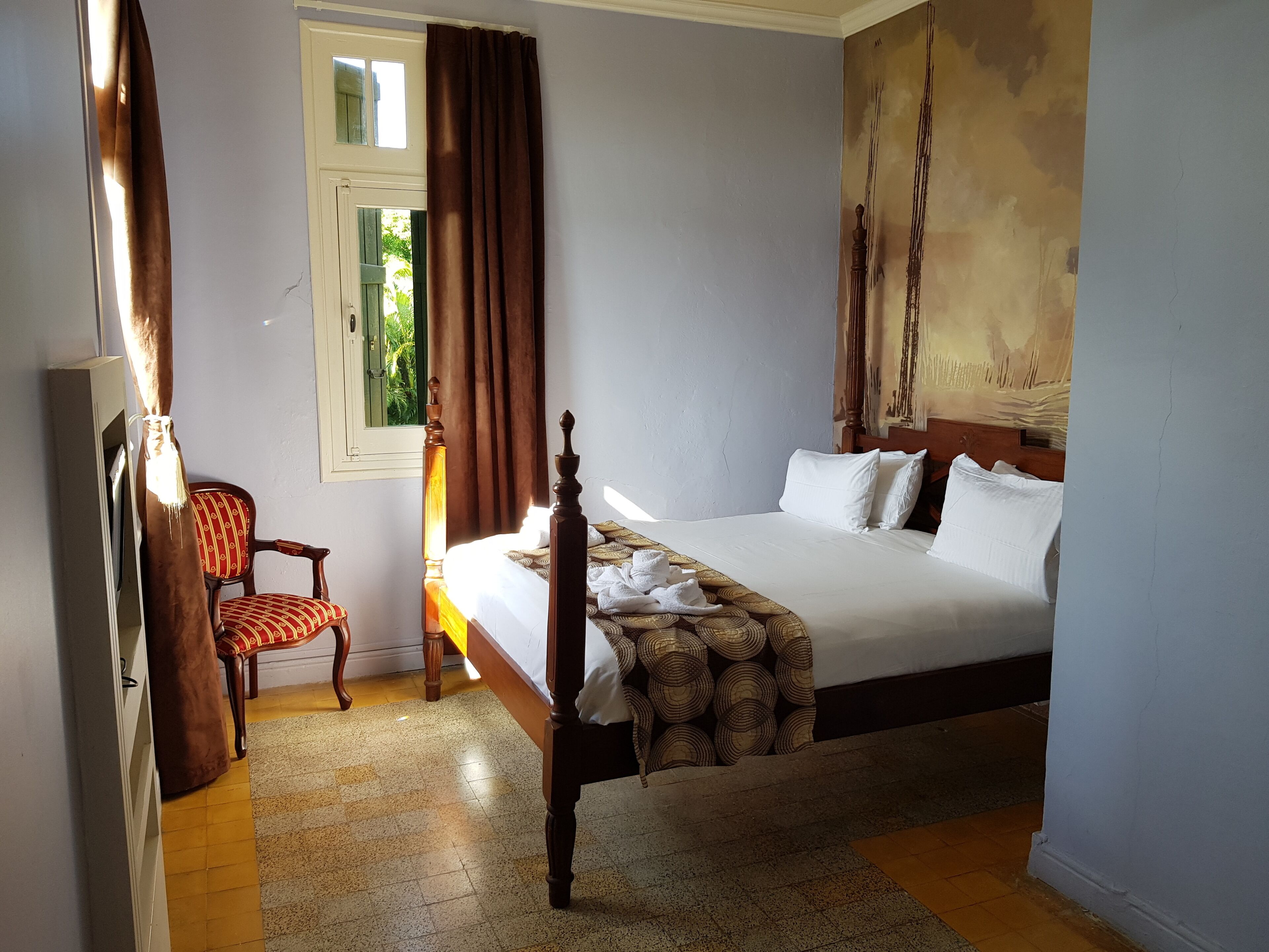 Un dormitorio con cama, una silla y una ventana con cortinas.