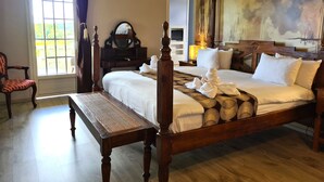 A well-lit bedroom with a large bed, a wooden nightstand, a dresser, a chair, and a large window. - Habitation du Comté (Sainte-Rose)