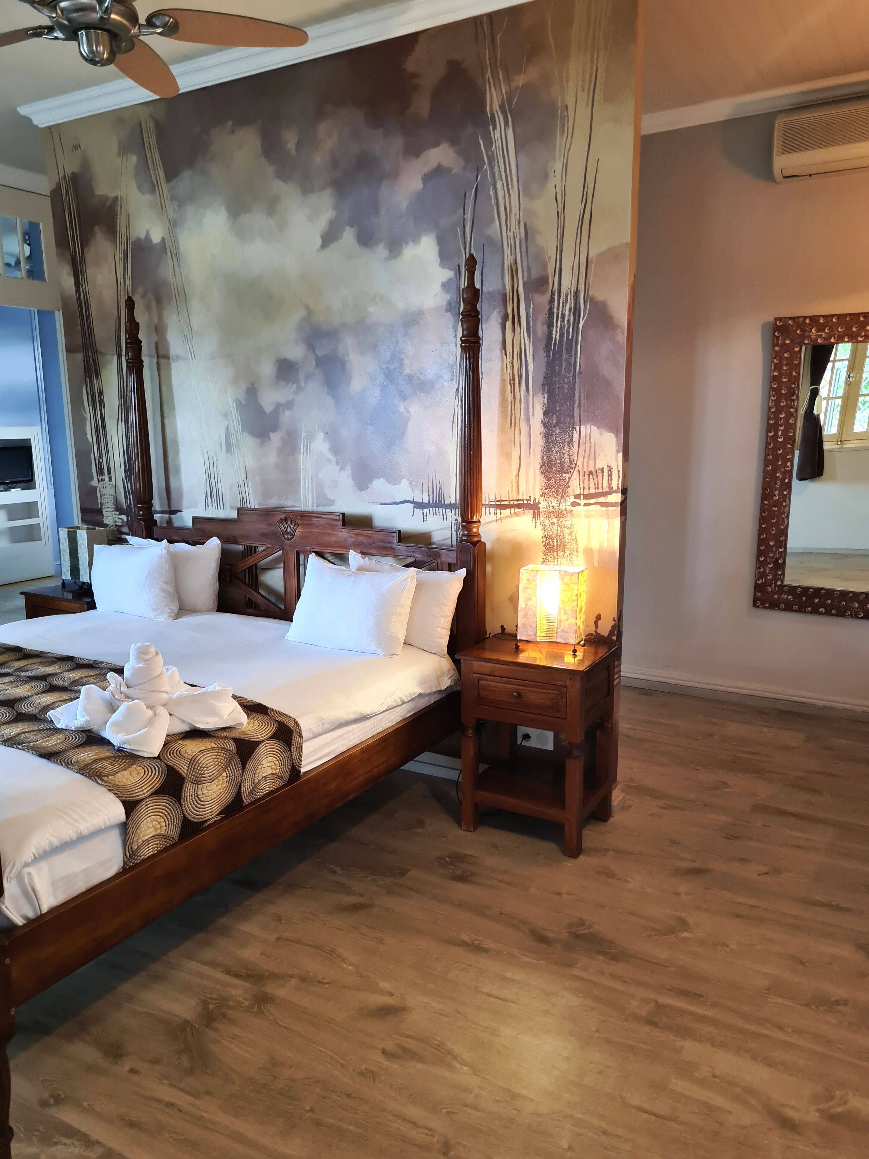 A hotel room with a large bed, a nightstand with a lamp, and a mural on the wall.