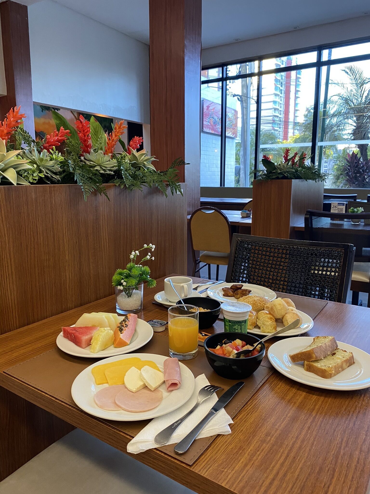 Una mesa de desayuno con diversos alimentos, una taza de café y un vaso de zumo de naranja.
