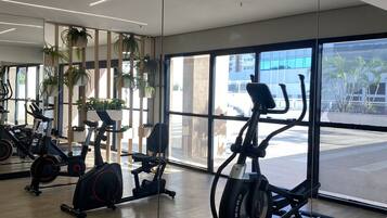 Uma academia com equipamentos de ginástica, amplas janelas e plantas em vasos.