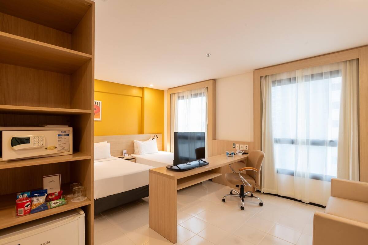 A hotel room with two beds, a desk, a chair, a TV, a microwave, and a minibar.