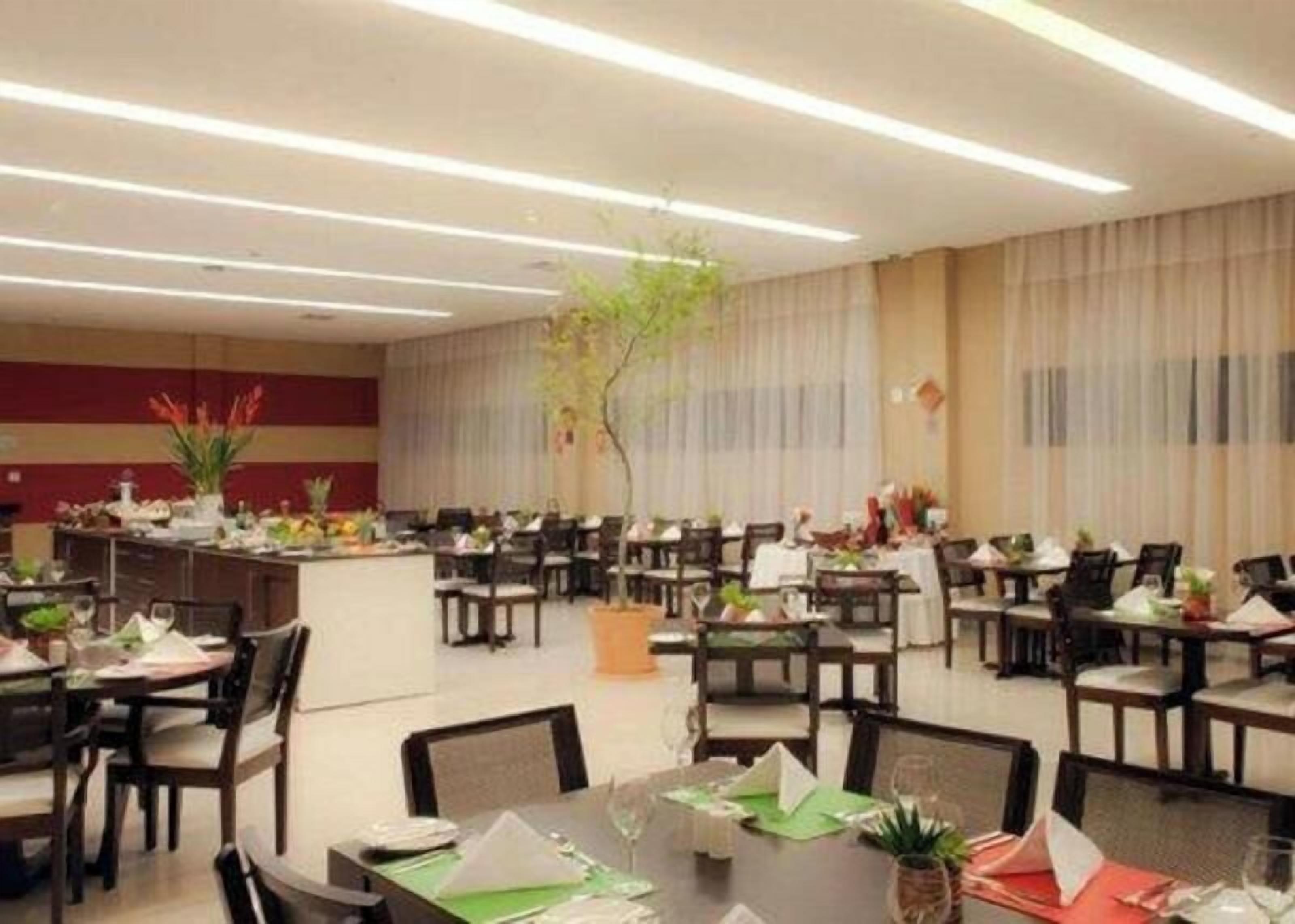 A hotel dining area with multiple tables and chairs, a central plant, and a long counter with a menu.
