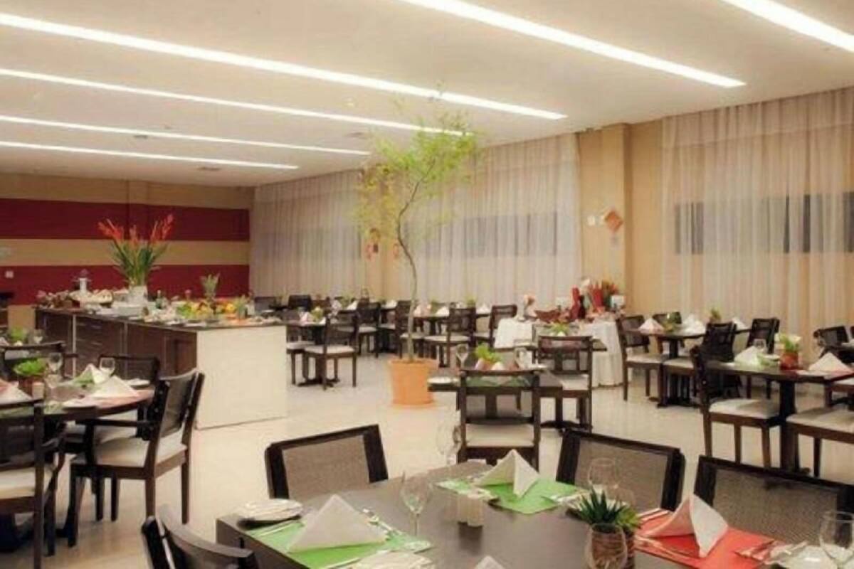A hotel dining area with multiple tables and chairs, a central plant, and a long counter with a menu.
