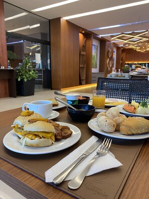 Un desayuno con sándwich, tostadas, fruta y un tazón de sopa.