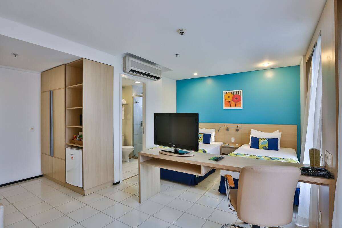 A hotel room with a bed, desk, chair, TV, wardrobe, and bathroom.