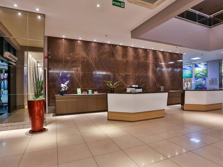 Un moderno vestíbulo de hotel con una recepción, una planta grande en maceta y una pared con obras de arte.