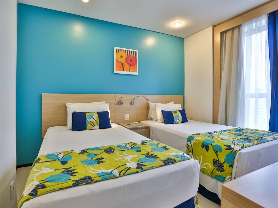 Habitación de hotel con dos camas, cabecero de madera, mesita de noche y un cuadro en la pared.
