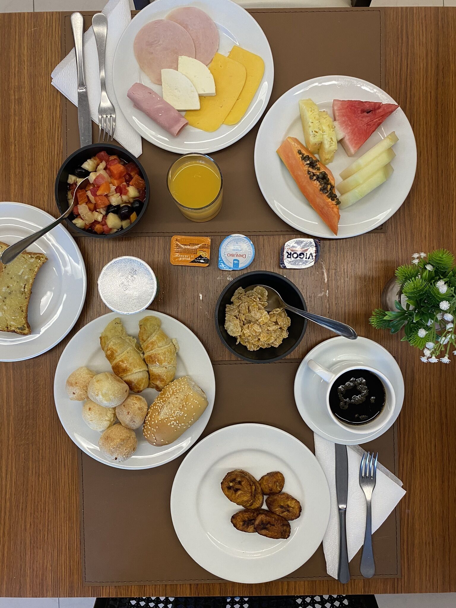 Una mesa de desayuno con platos de jamón, queso, fruta, croissants y bollería.