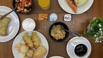 Una mesa de desayuno con platos de jamón, queso, fruta, croissants y bollería.