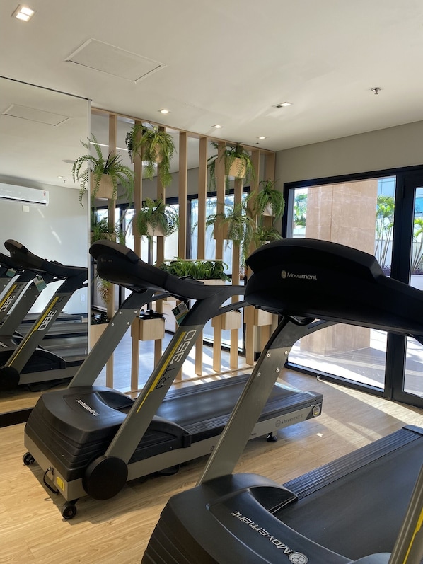 A gym with treadmills, wooden flooring, and large windows with a view of palm trees.