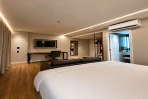 Una habitación de hotel moderna con una cama grande, un escritorio con silla, un televisor de pantalla plana y un equipo de aire acondicionado.
