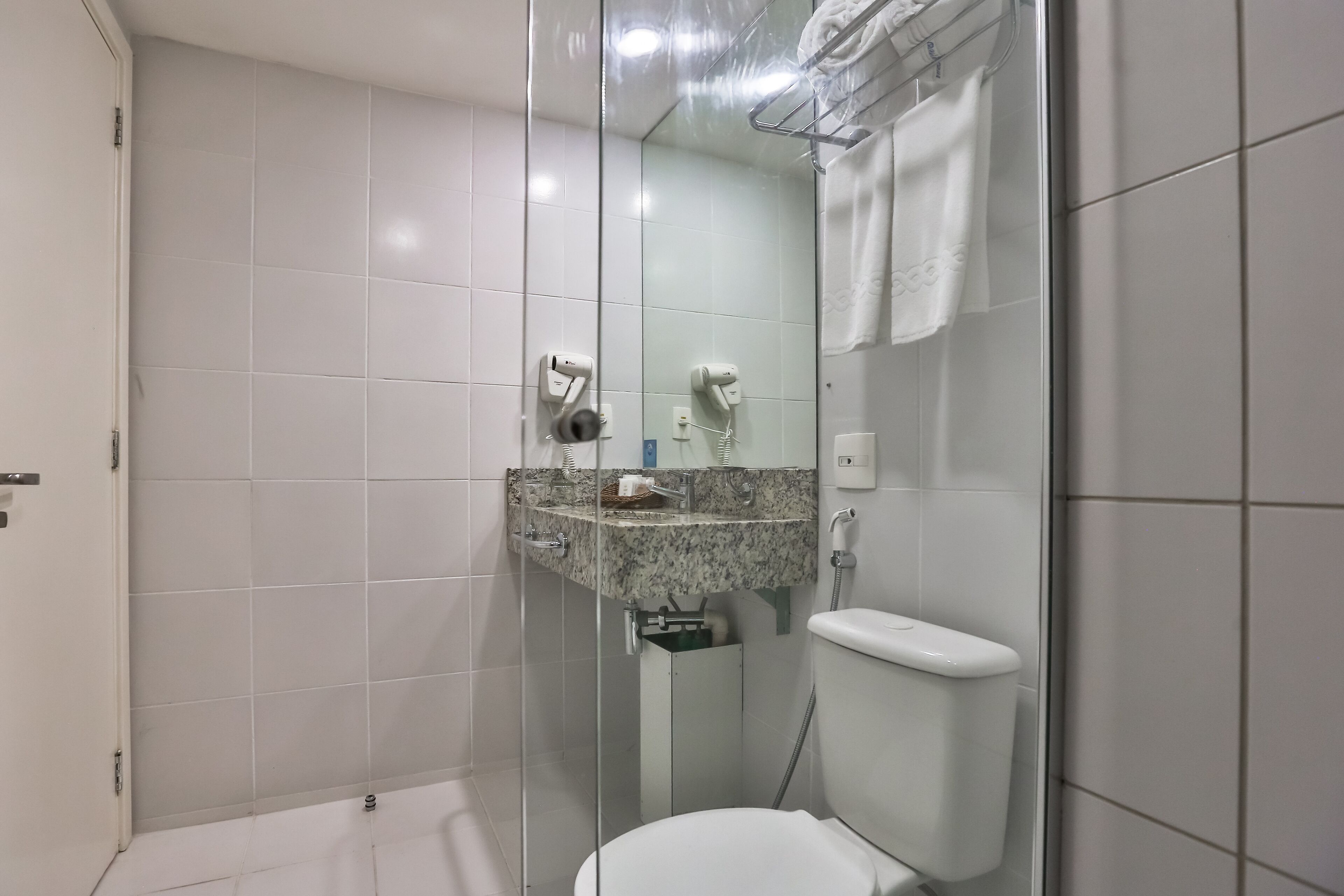 Une salle de bain moderne avec une douche à parois de verre, des toilettes blanches et un lavabo en marbre surmonté d’un porte-serviettes.