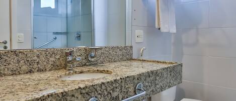 A bathroom with a granite countertop, a toilet, a shower, and a towel rack.