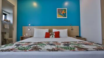 Quarto de hotel com cama, parede azul decorativa, um quadro e cabeceira de madeira.