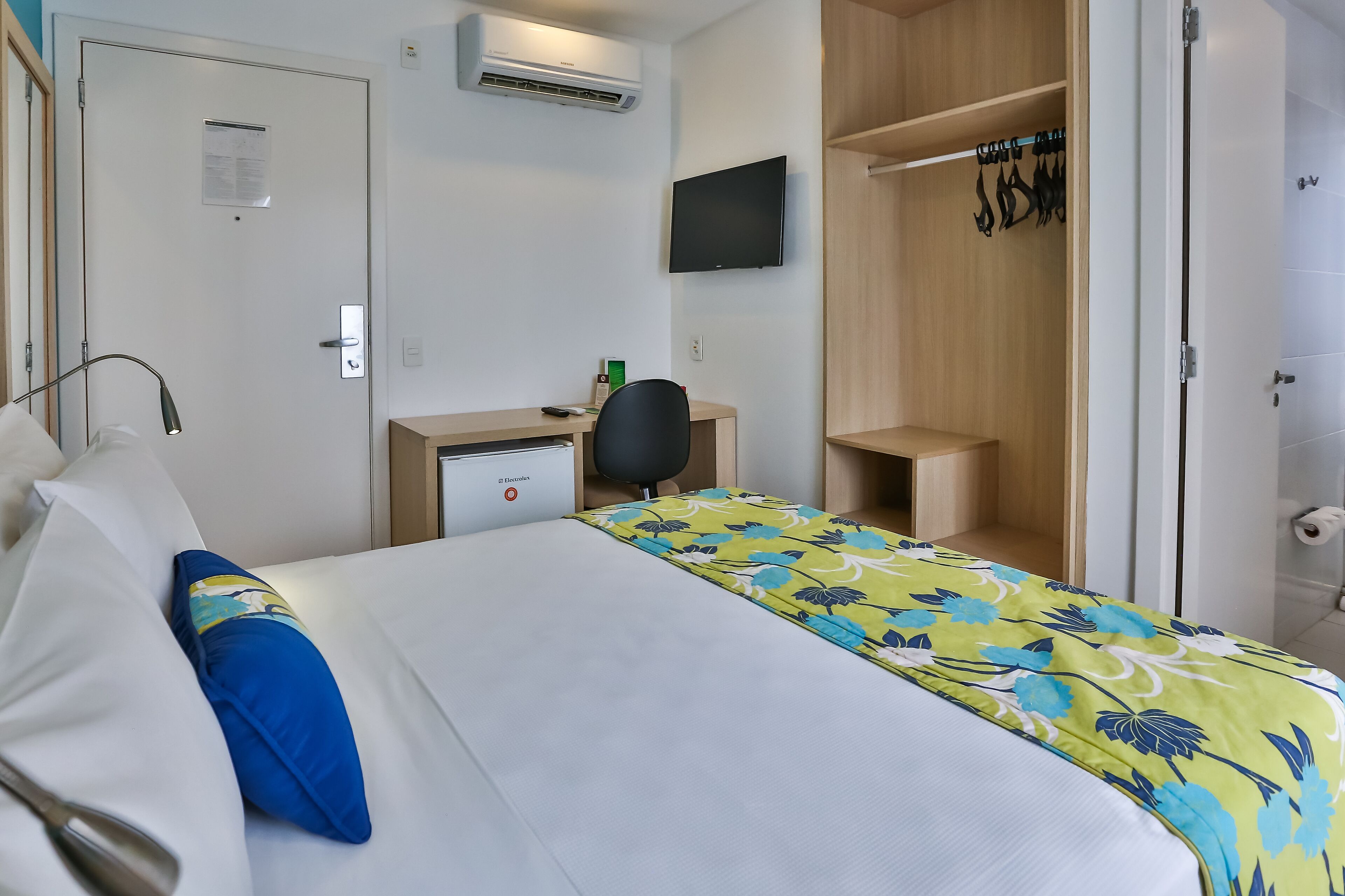 Habitación de hotel con cama, escritorio, silla, televisor y armario.