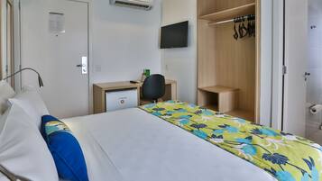 A hotel room with a bed, a desk, a chair, a TV, and a wardrobe.
