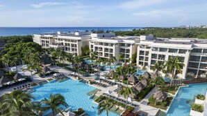 A resort with a large swimming pool, multiple lounge areas, and a view of the ocean.