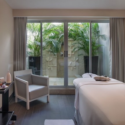 A modern hotel room with a bed, a seating area, and a view of a garden through a sliding glass door.