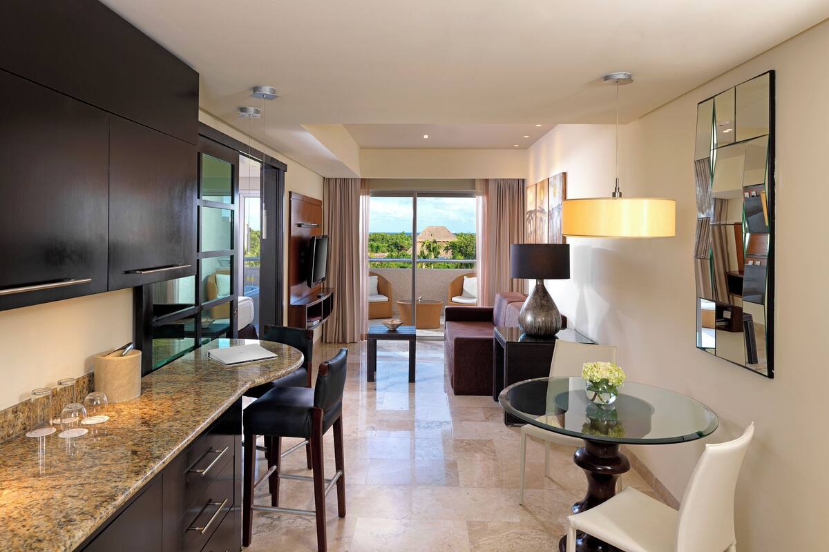 A modern kitchen with a dining area, a glass-top table, and a view of the outdoors.