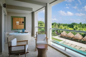Un balcón con vista a una piscina y sombrillas de paja, un jacuzzi, muebles de mimbre y una obra de arte enmarcada en la pared.