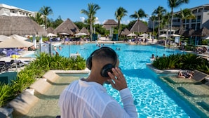 A pool area with lounge chairs and umbrellas, surrounded by palm trees and thatched-roof structures.