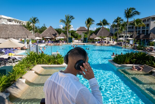 A pool area with lounge chairs and umbrellas, surrounded by palm trees and thatched-roof structures. - Paradisus La Perla - Adults Only - Riviera Maya - All Inclusive (Playa del Carmen)