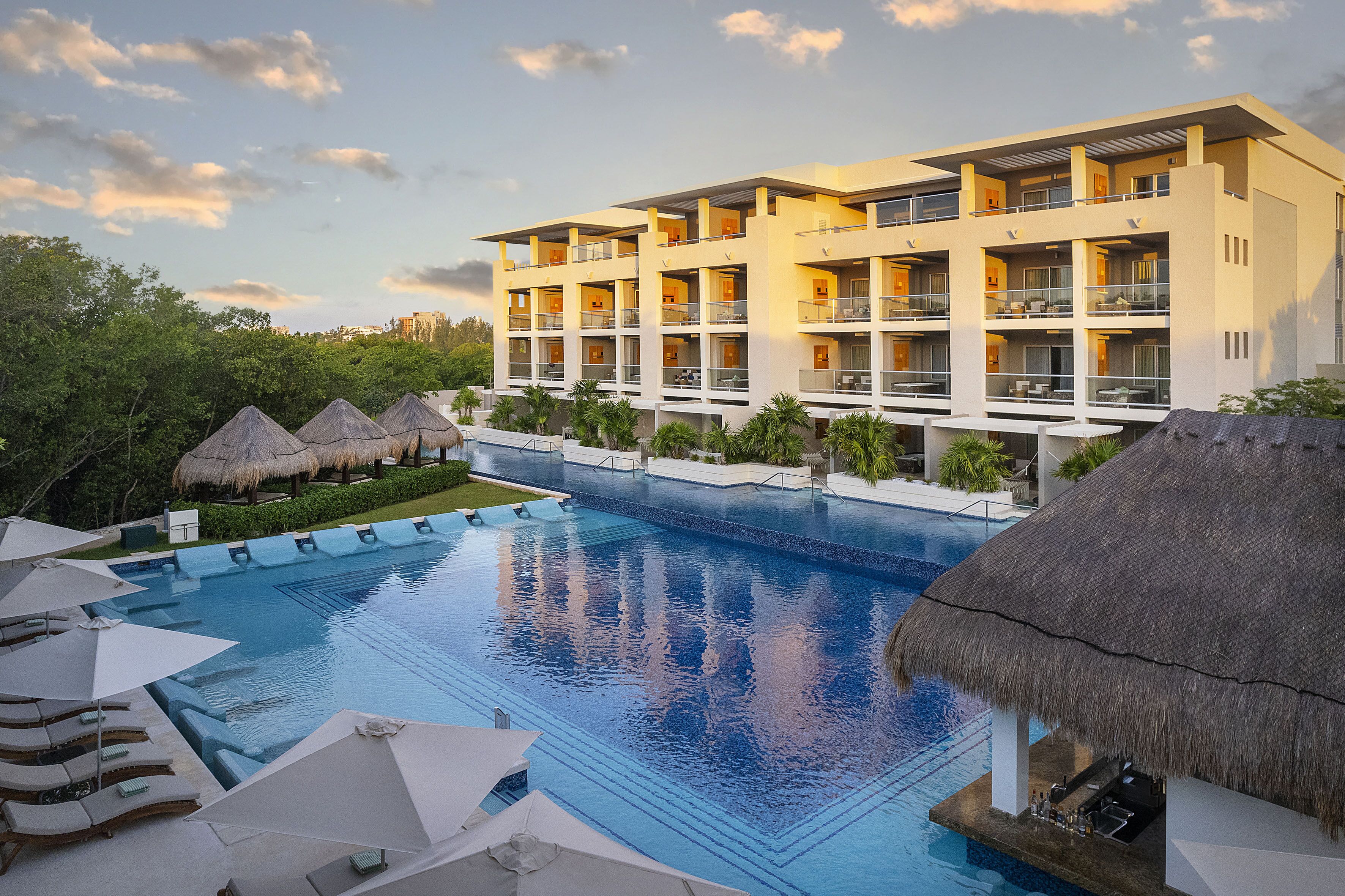 Un hotel con piscina, construcciones de techo de paja y un edificio de varios pisos con balcones.