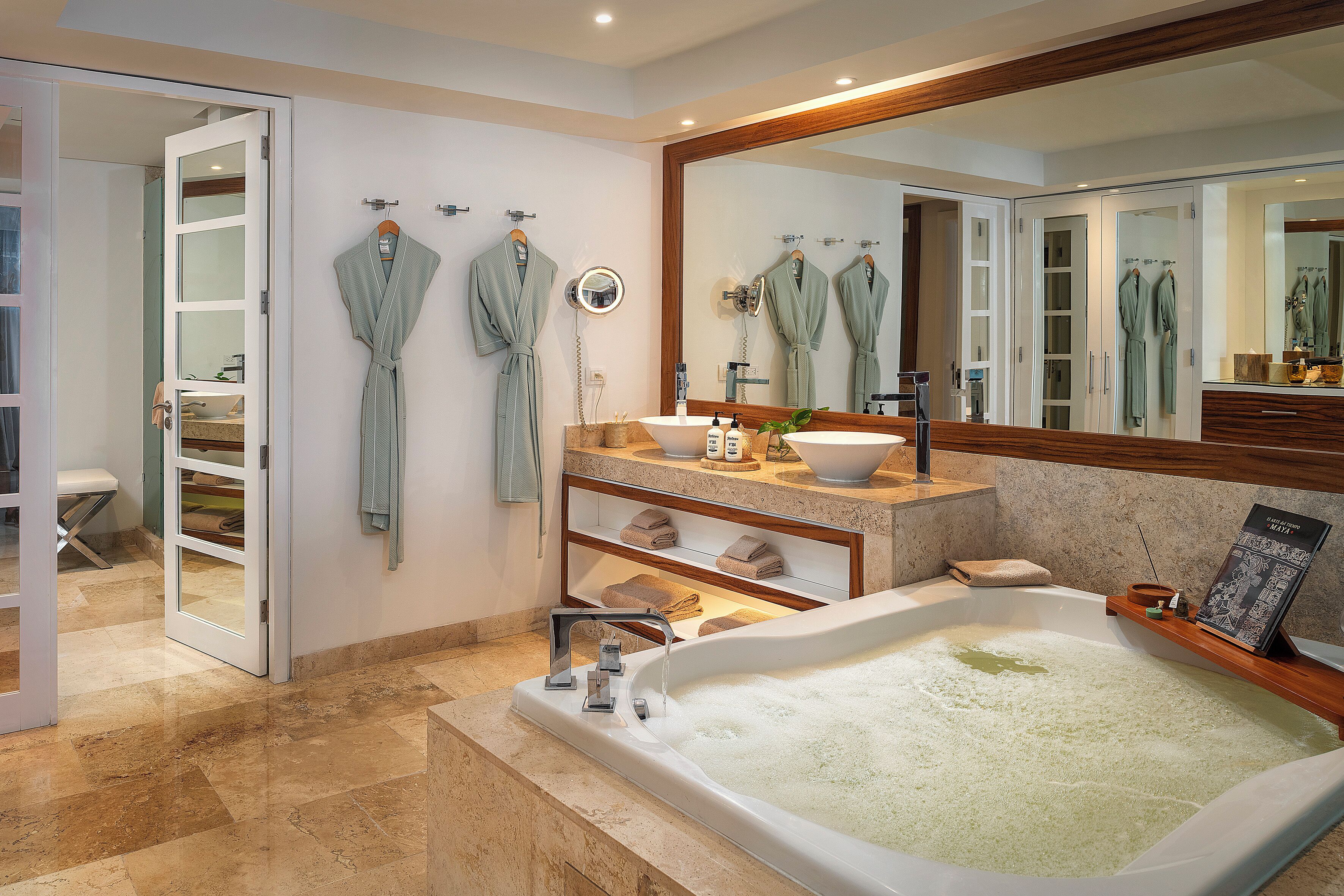 A modern bathroom with a bathtub, a vanity with a mirror, and two robes hanging on hooks.