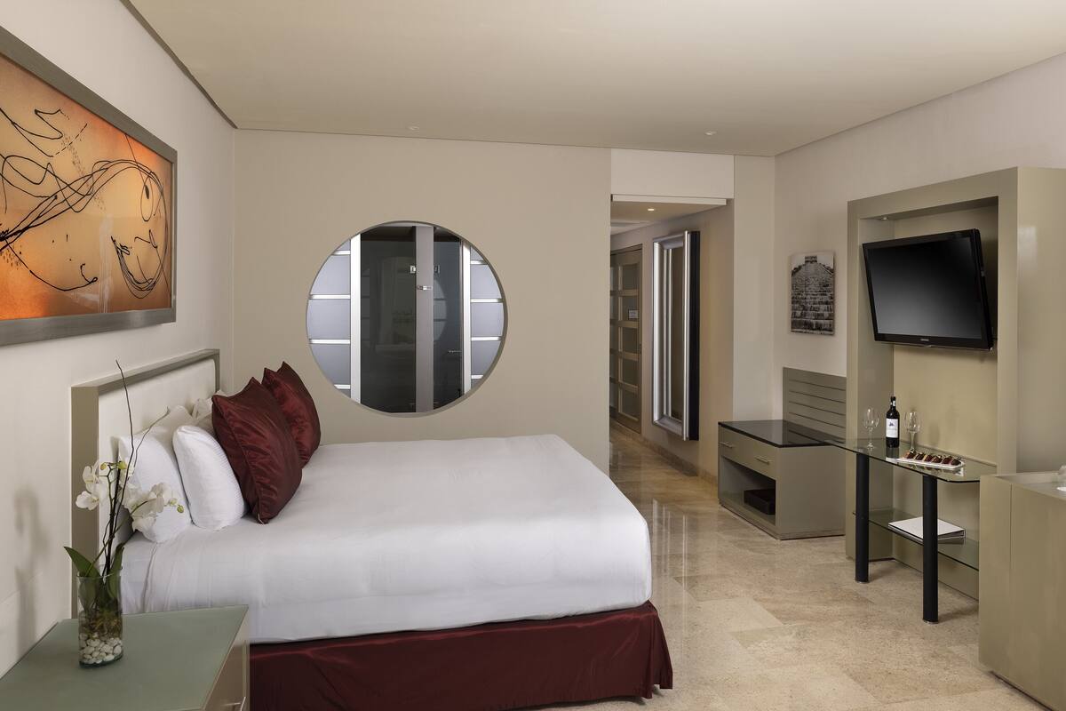A hotel room with a bed, a desk, a TV, and a minibar.