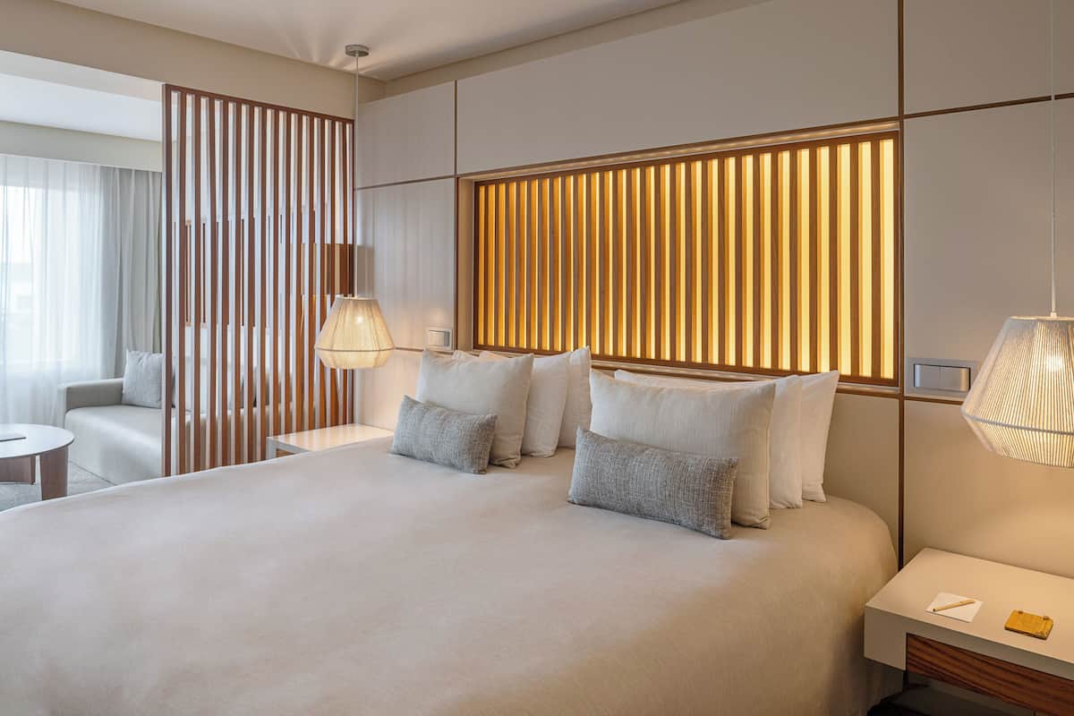 A modern hotel room with a large bed, bedside lamps, a wooden headboard, and a view of the city.