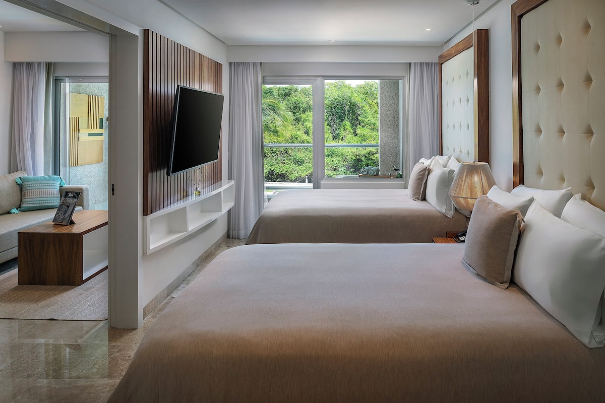 A modern hotel room with a large bed, a TV, and a balcony with a view of greenery.