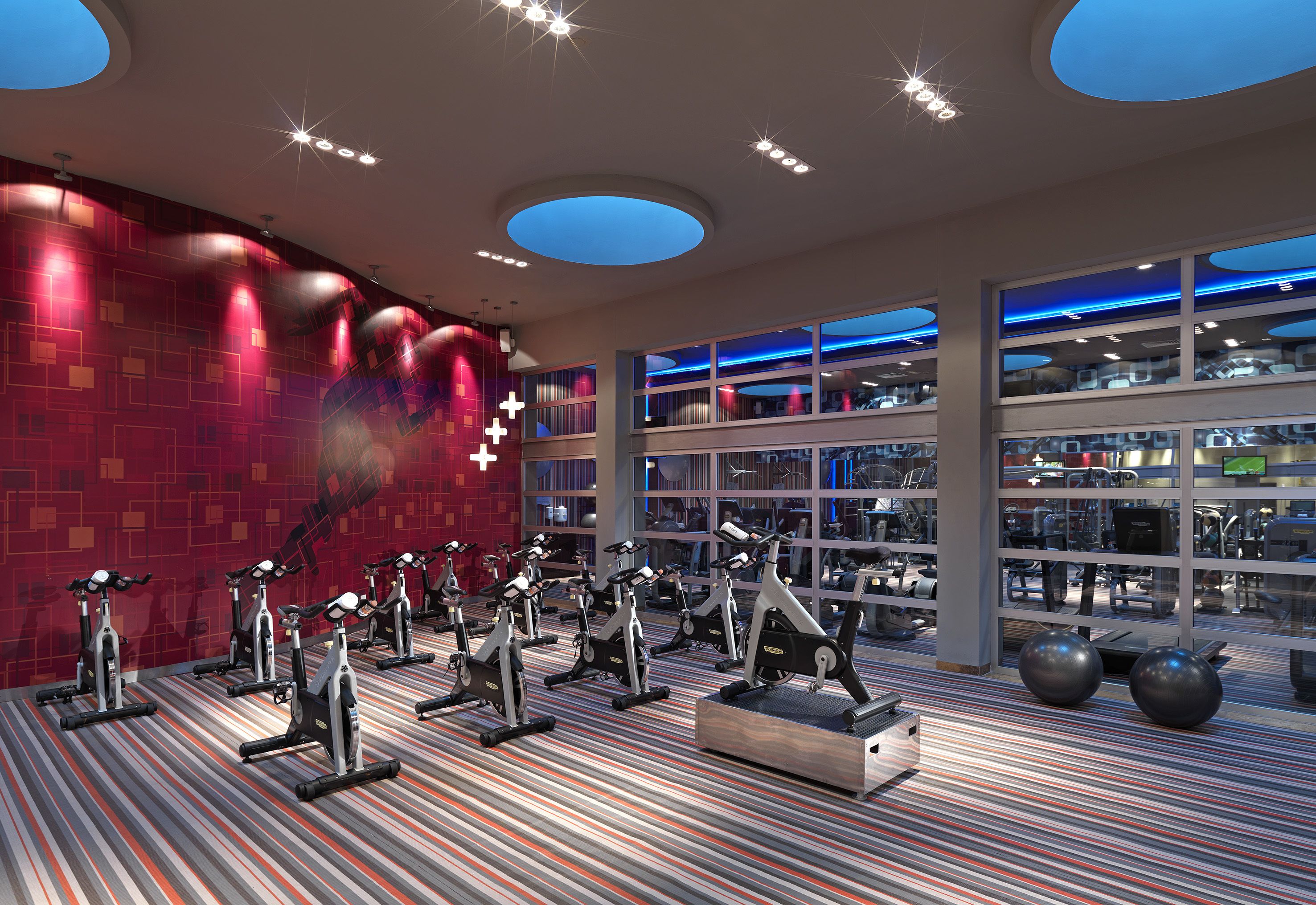 Un gimnasio con bicicletas estáticas, una alfombra estampada y ventanas amplias.