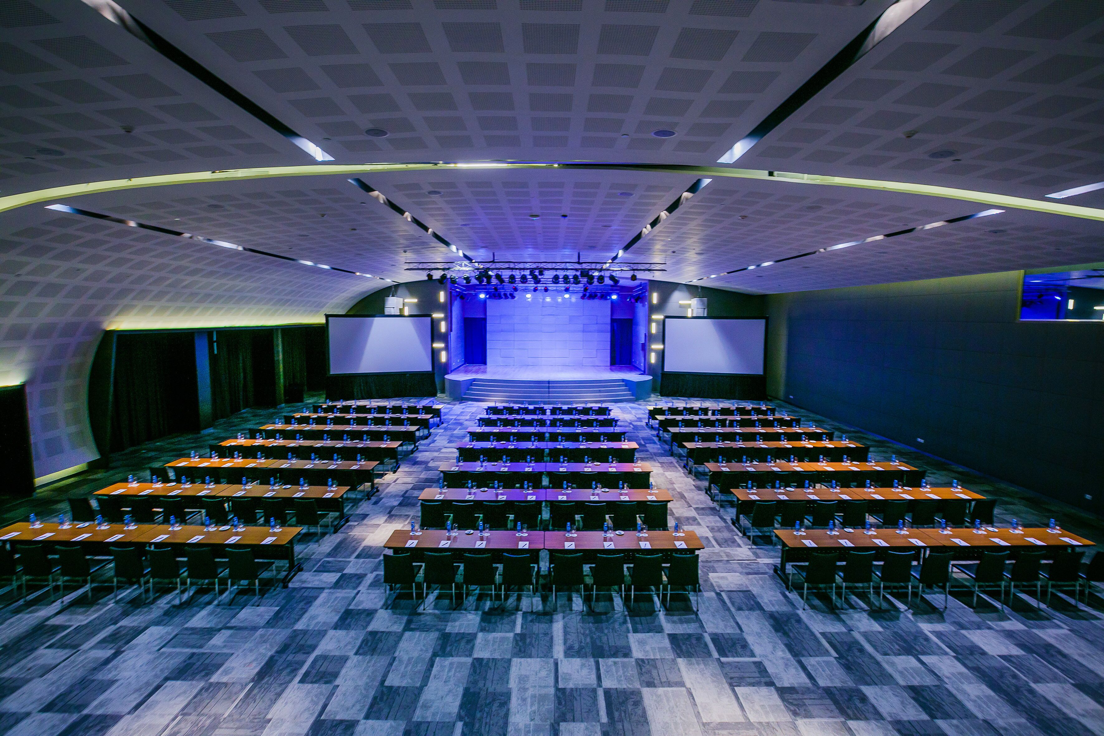 A conference room with a stage, rows of tables, and chairs.